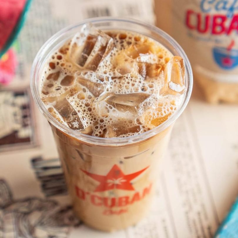 Iced D'Cuban Cafe coffee with ice and foam in a clear plastic cup.