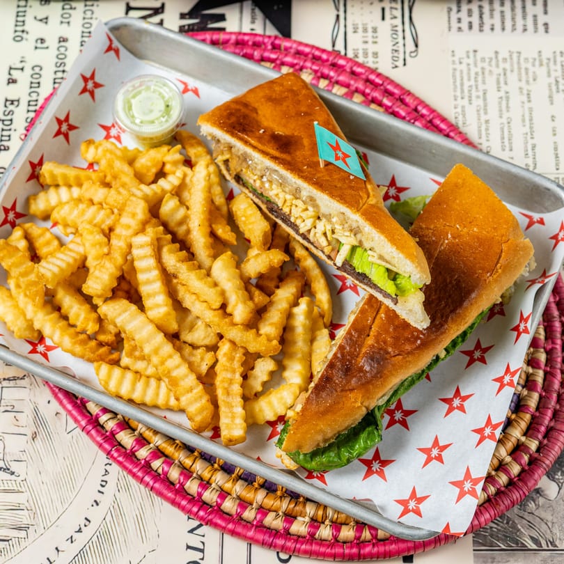 A D'Cuban Cafe Cuban sandwich with fries and dipping sauce on a metal tray.