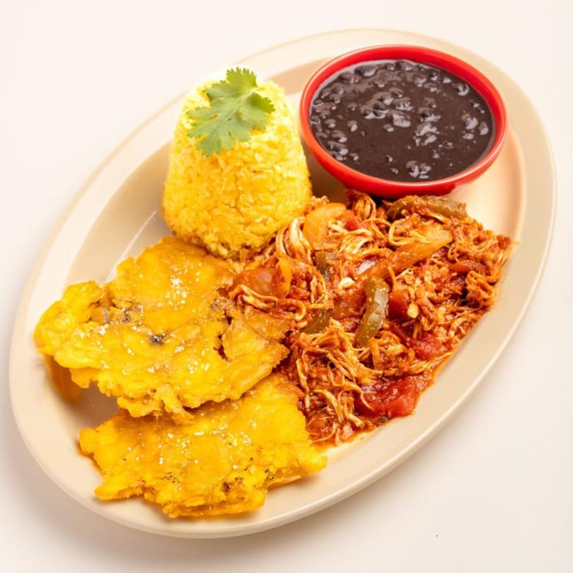 A Cuban dish with yellow rice, black beans, shredded chicken, and two fried plantains.